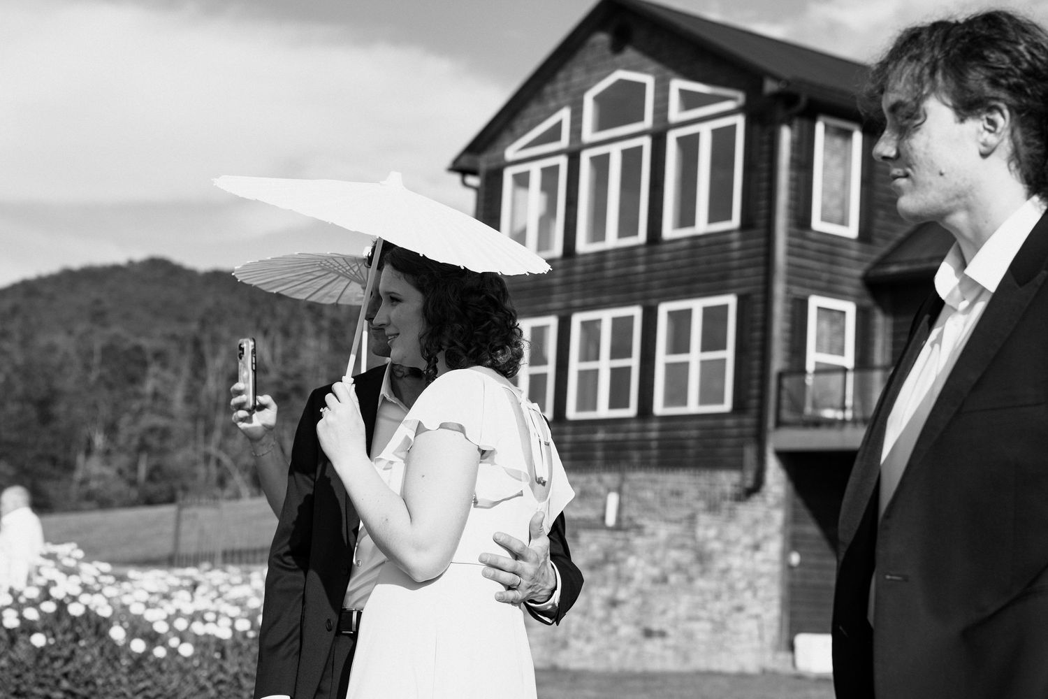 A series of black and white wedding photographs showing candid moments in front of rustic buildings and mountain scenery.