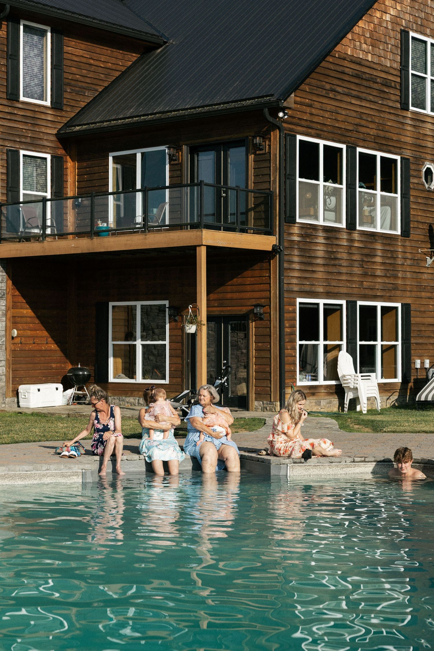 Wedding guests relax and socialize in a resort pool with rustic wooden lodge buildings in the background.
