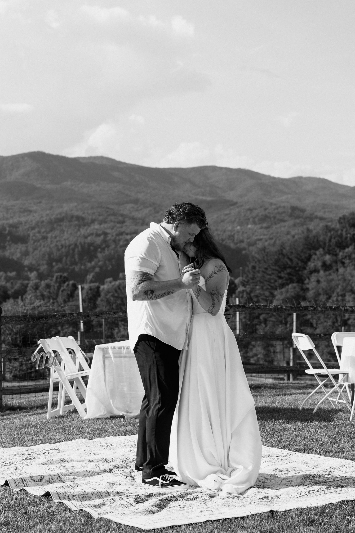 A romantic outdoor prayer scene with a couple kneeling on a blanket against a mountain backdrop in black and white.