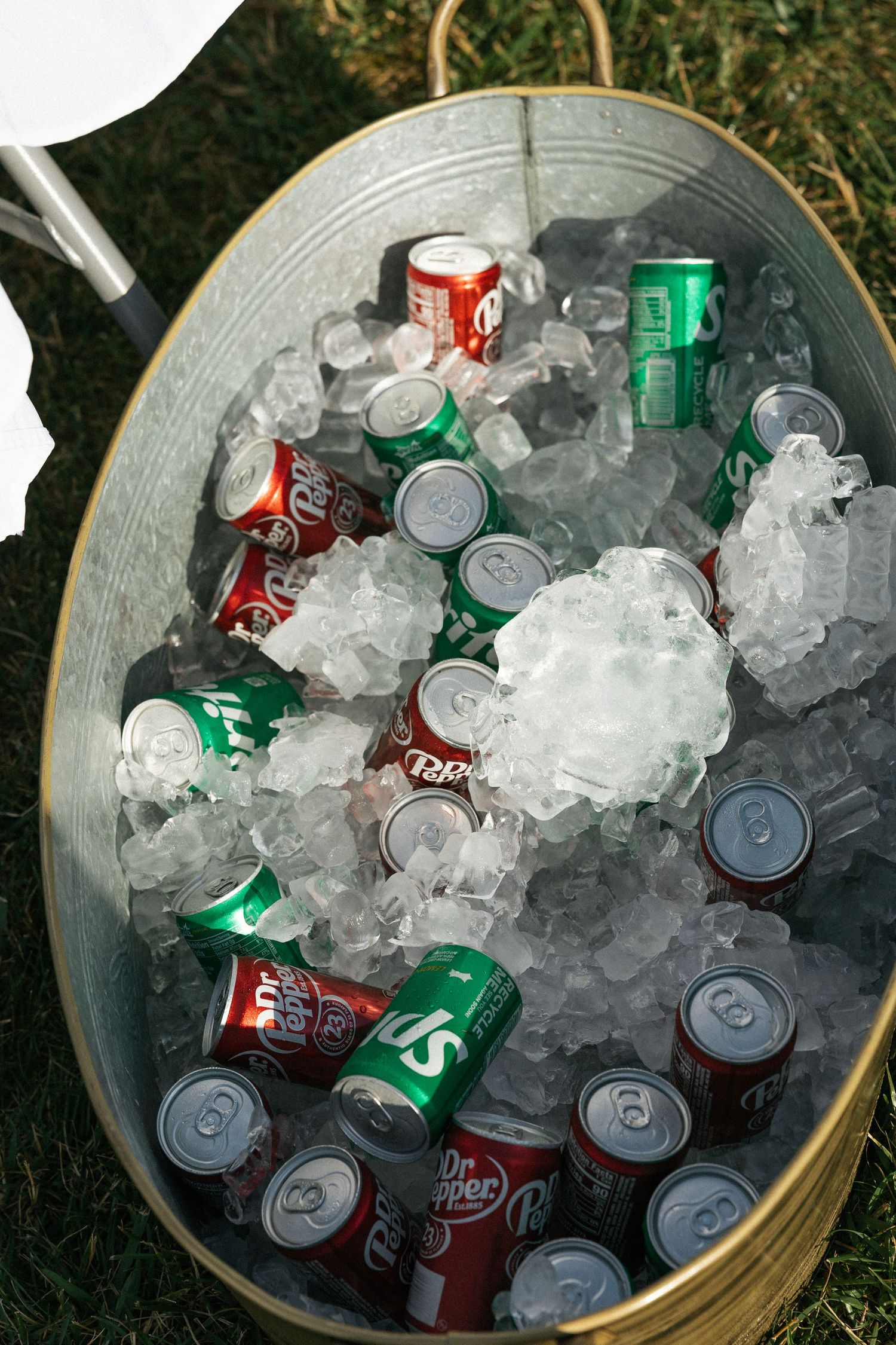 Ice-filled bucket with red and green soda cans chilling at an outdoor event.