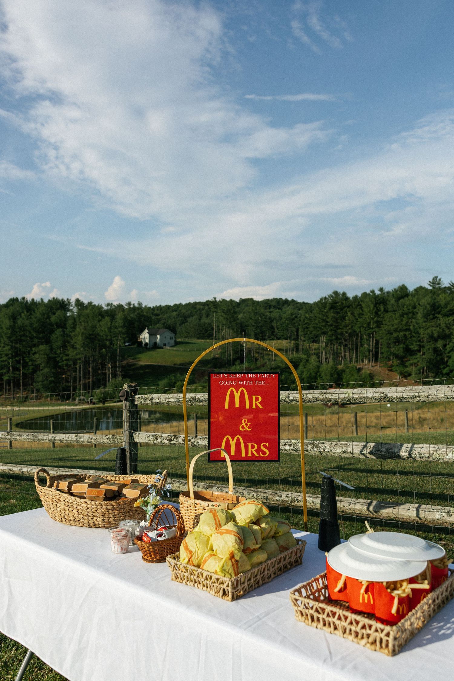 Decorative wedding dessert displays with 'Mr' and 'Mrs' signs arranged on white tables against a scenic outdoor backdrop.