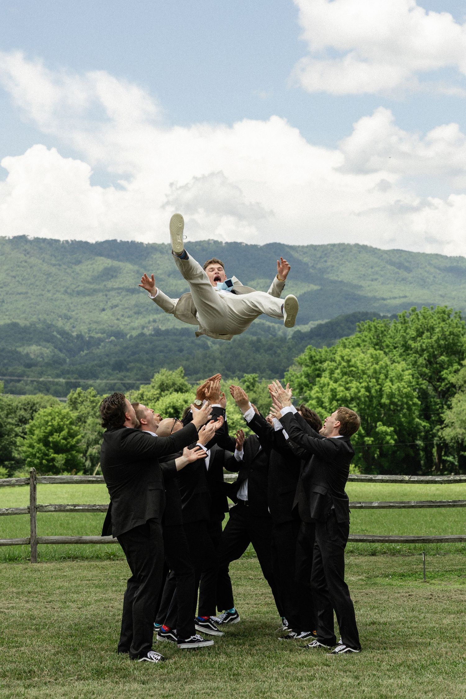 A celebratory group toss at a graduation ceremony with mountains in the background.