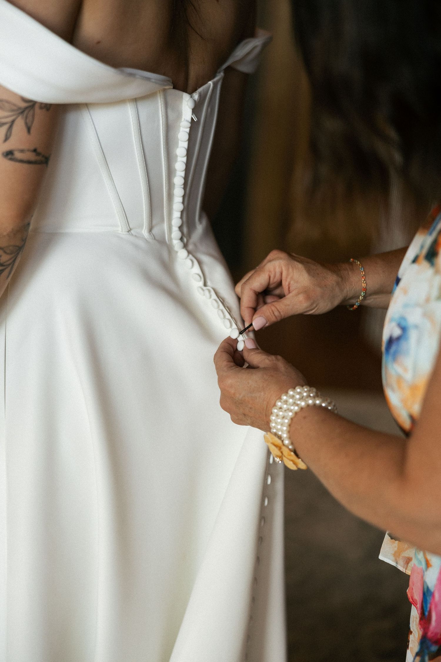 Close-up detail of someone adjusting a pearl bracelet on a white wedding dress sleeve.Micro wedding, elopement, intentional celebration