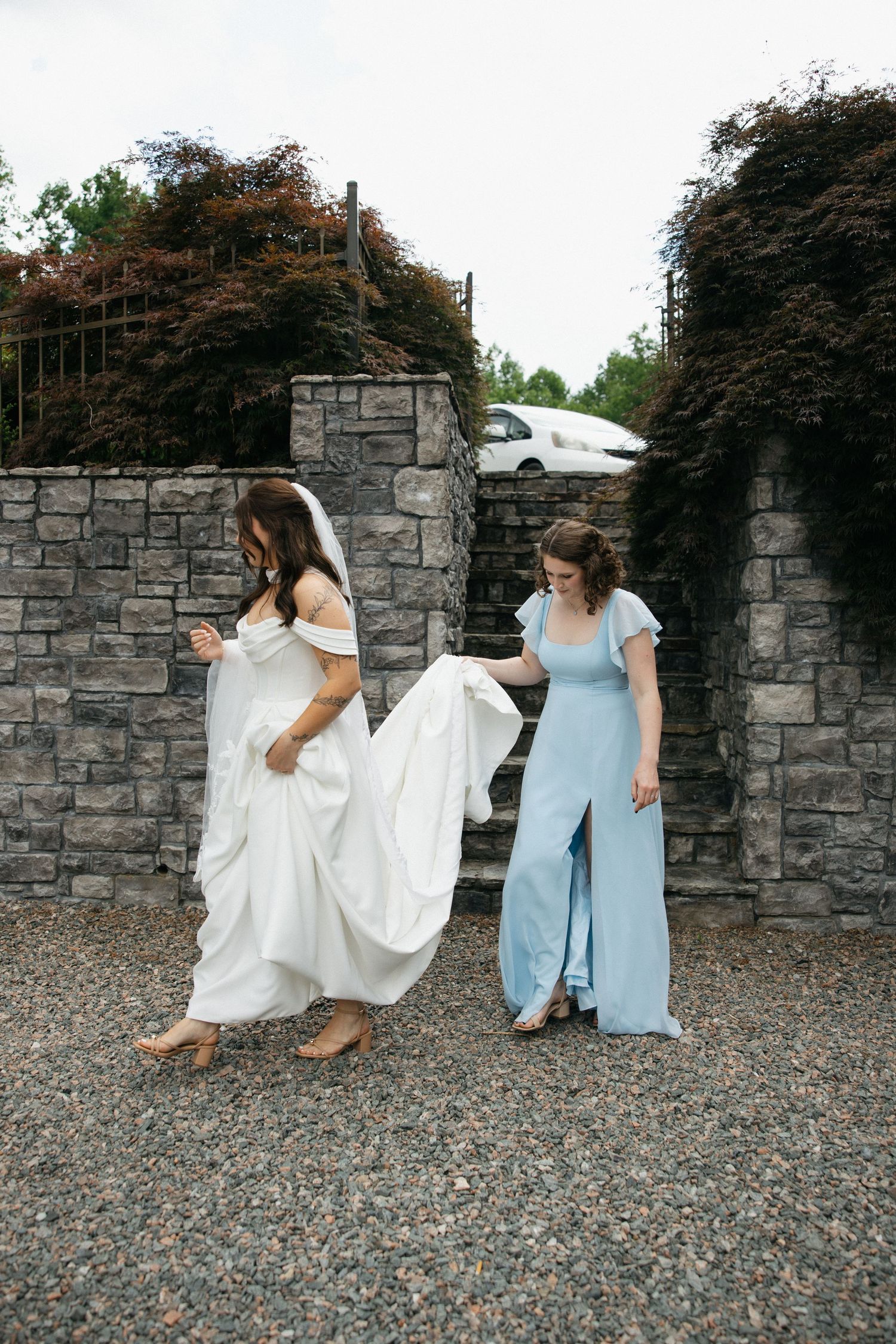 Two people in blue and white dresses sit together on a stone wall in a casual outdoor photoshoot series.