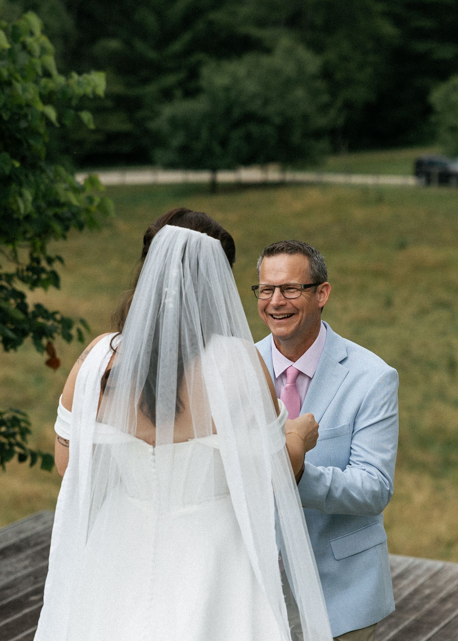 A wedding couple shares a special moment on a wooden deck with a pastoral green landscape in the background.
