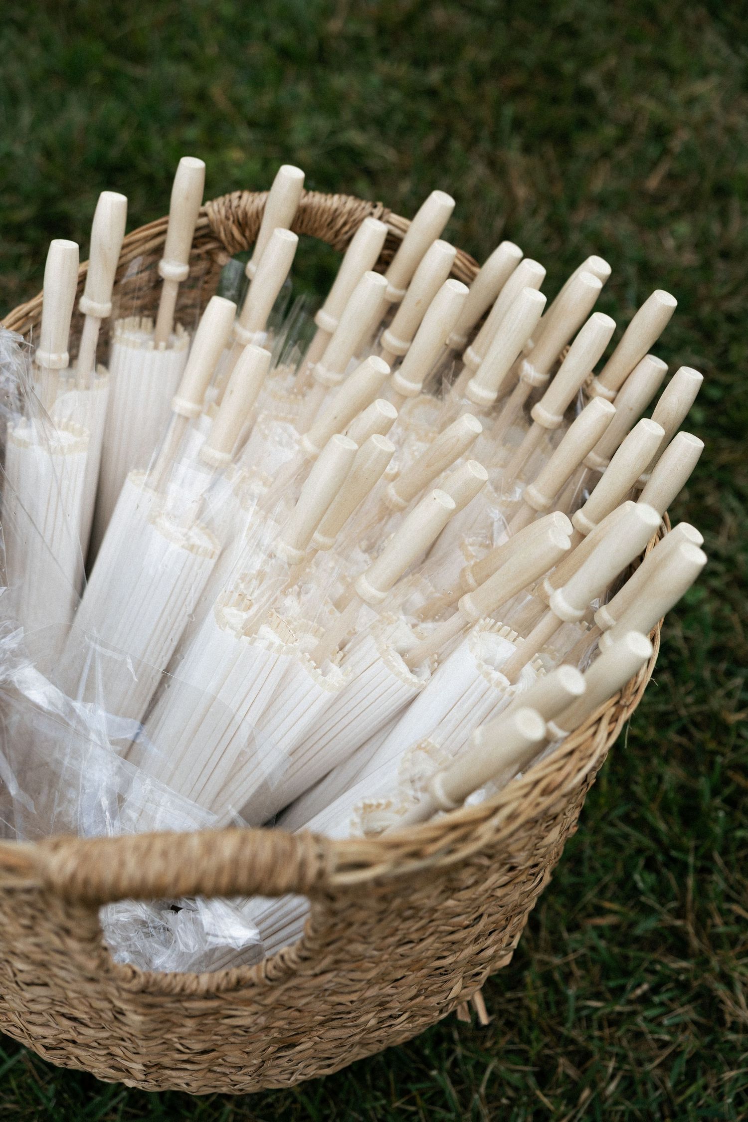 White paper parasols arranged in a woven basket on grass.Micro wedding, elopement, intentional celebration