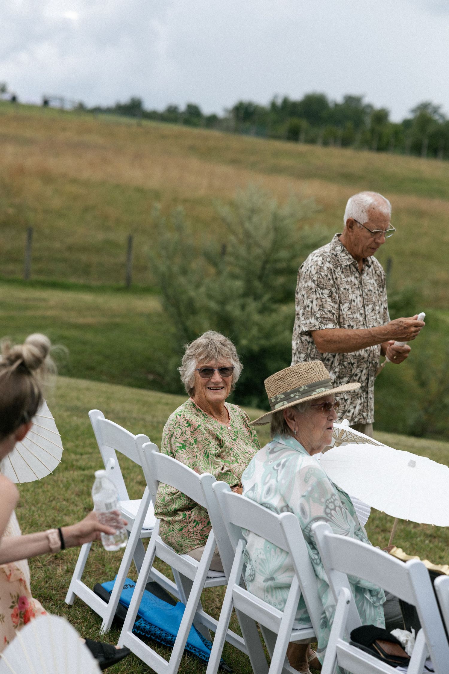 Wedding guests seated in white chairs outdoors on a grassy hillside.Micro wedding, elopement, intentional celebration