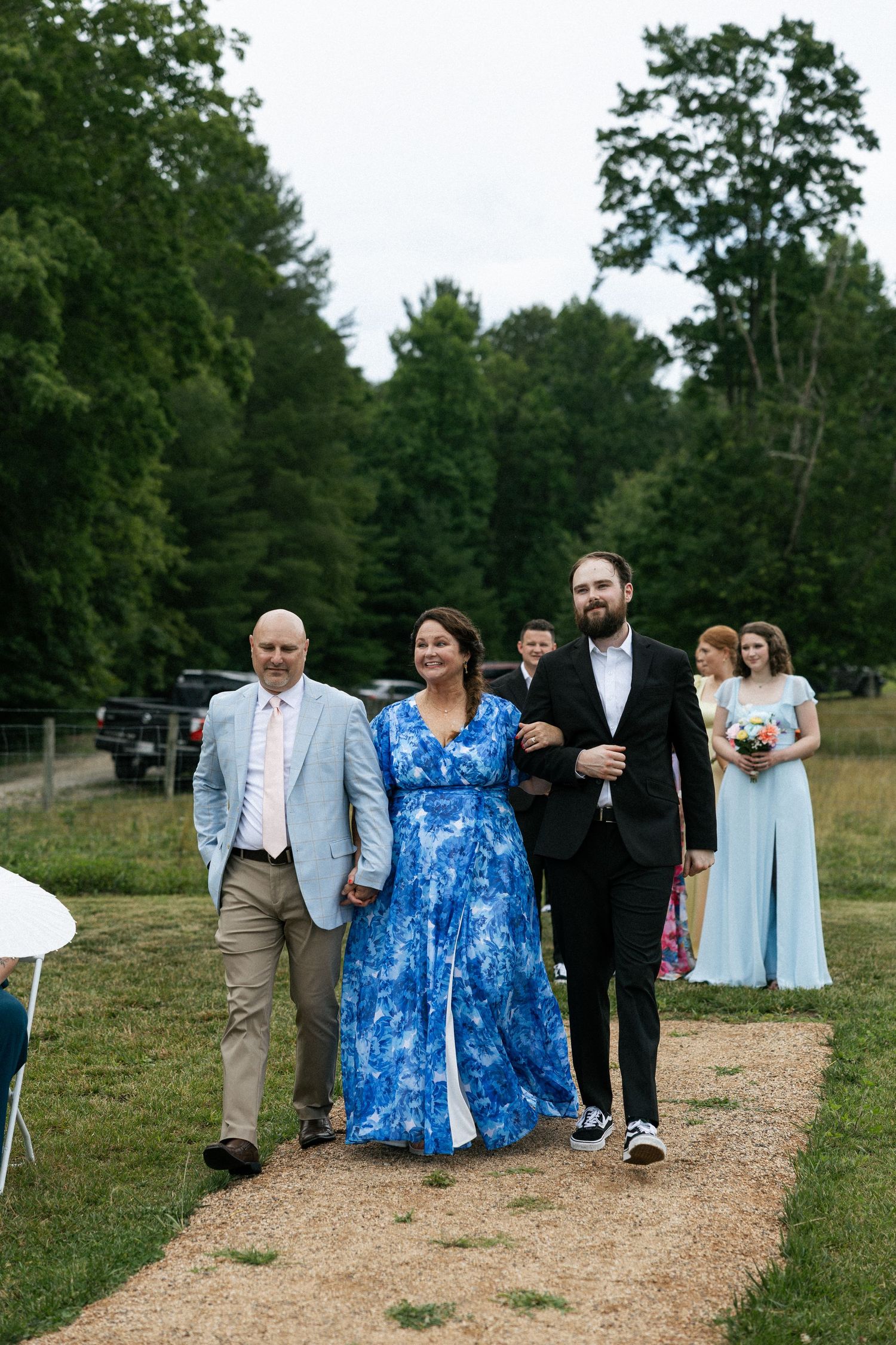 Wedding party members walk down a dirt path with trees in the background.Micro wedding, elopement, intentional celebration