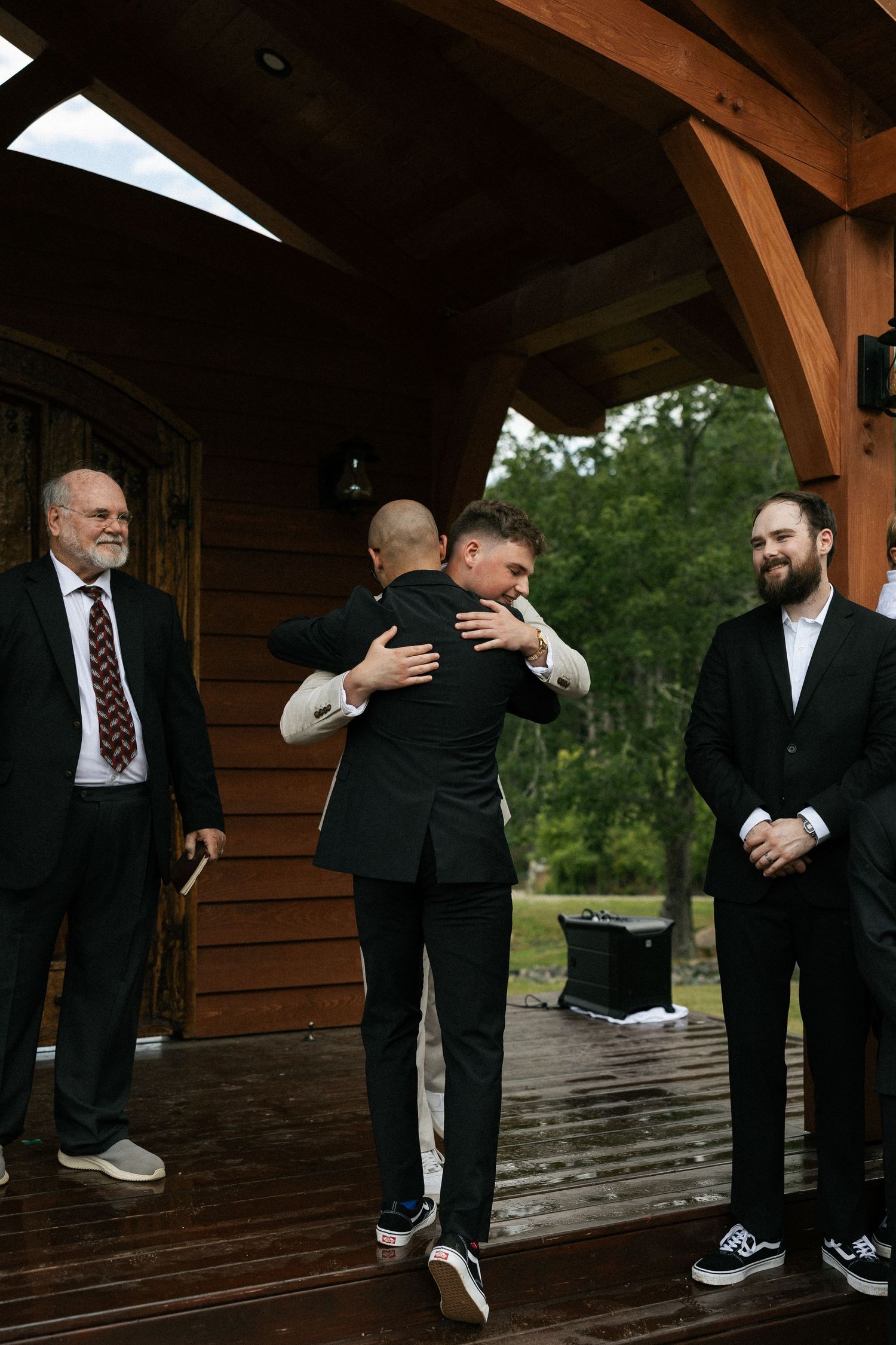 Wedding party members share embraces and laughter under a wooden pavilion.Micro wedding, elopement, intentional celebration