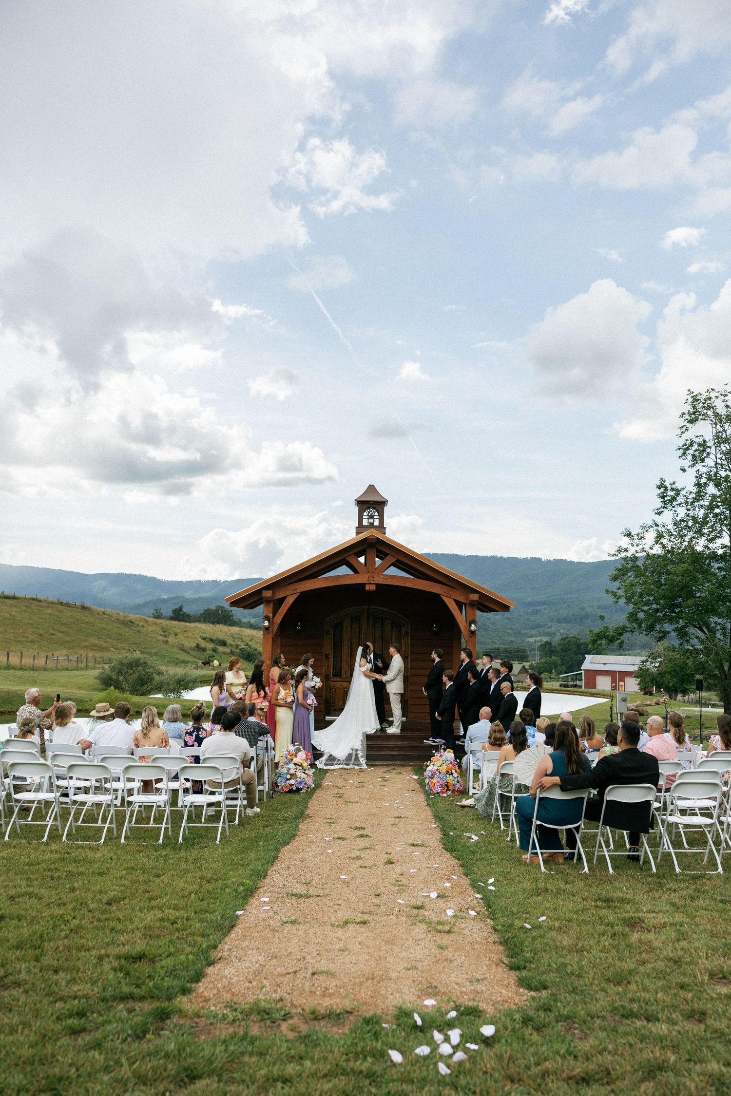 Outdoor wedding ceremony setup with wooden pavilion and white chairs against mountain backdrop.Micro wedding, elopement, intentional celebra