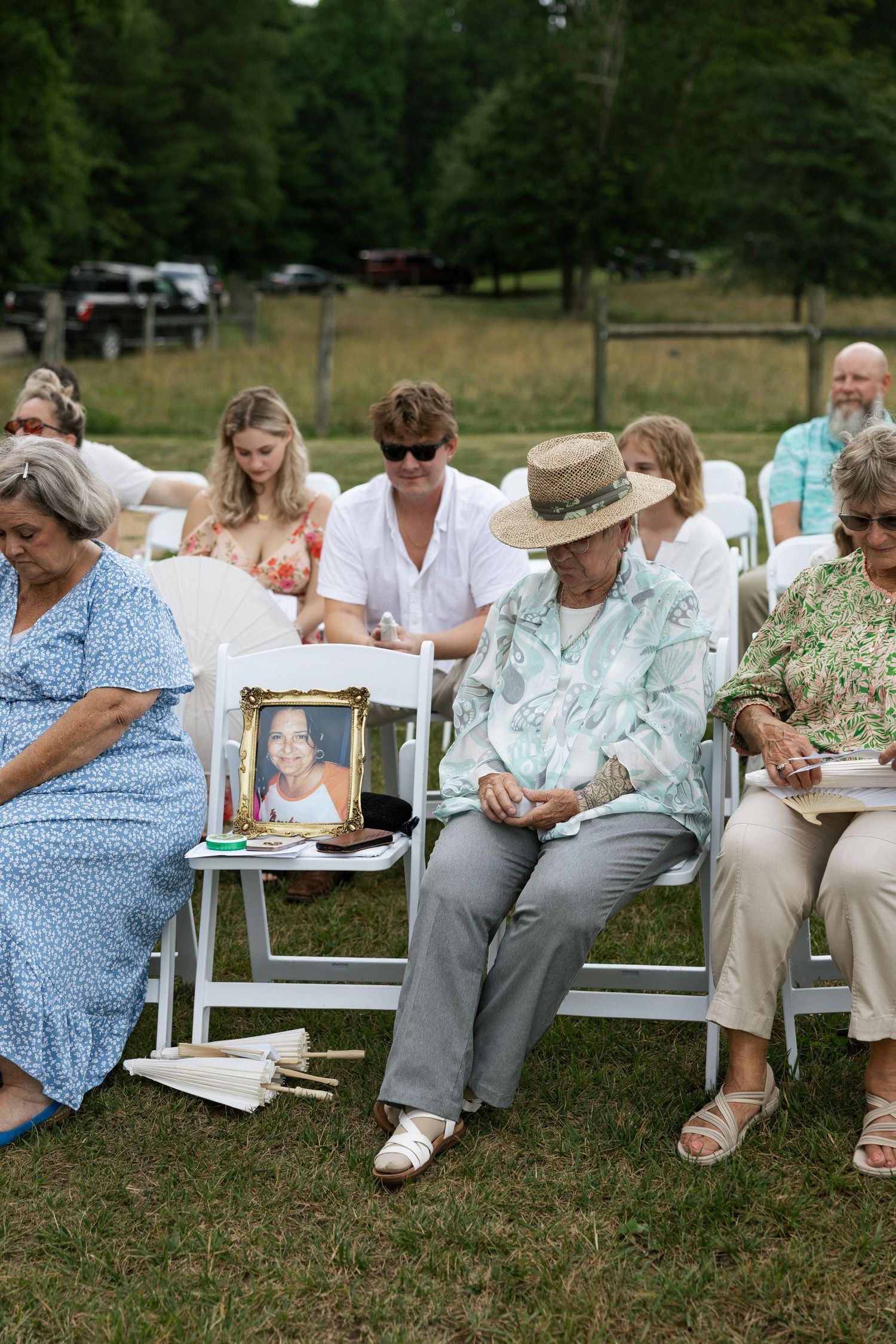 A group of people sit in white chairs on a lawn while taking notes during an outdoor gathering.Micro wedding, elopement, intentional celebra
