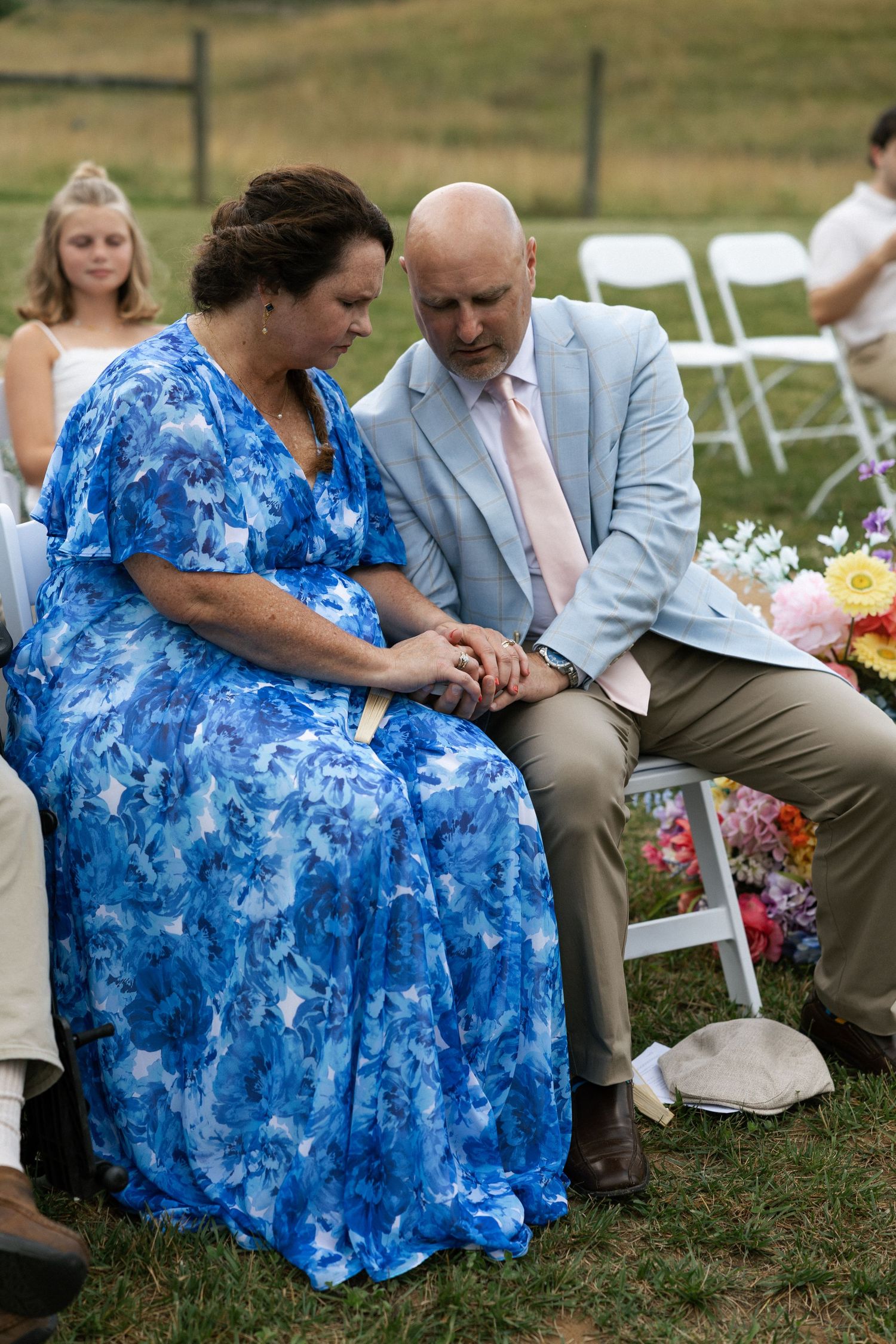 Two guests in formal attire share a quiet moment during an outdoor wedding ceremony.