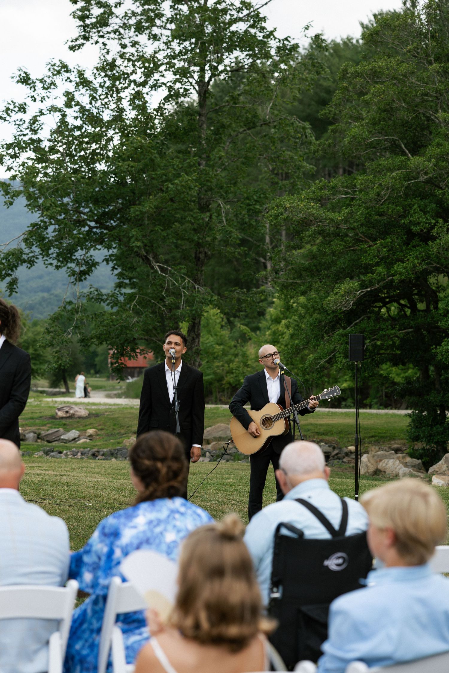 Musicians perform at an outdoor wedding ceremony with guests seated on white chairs.