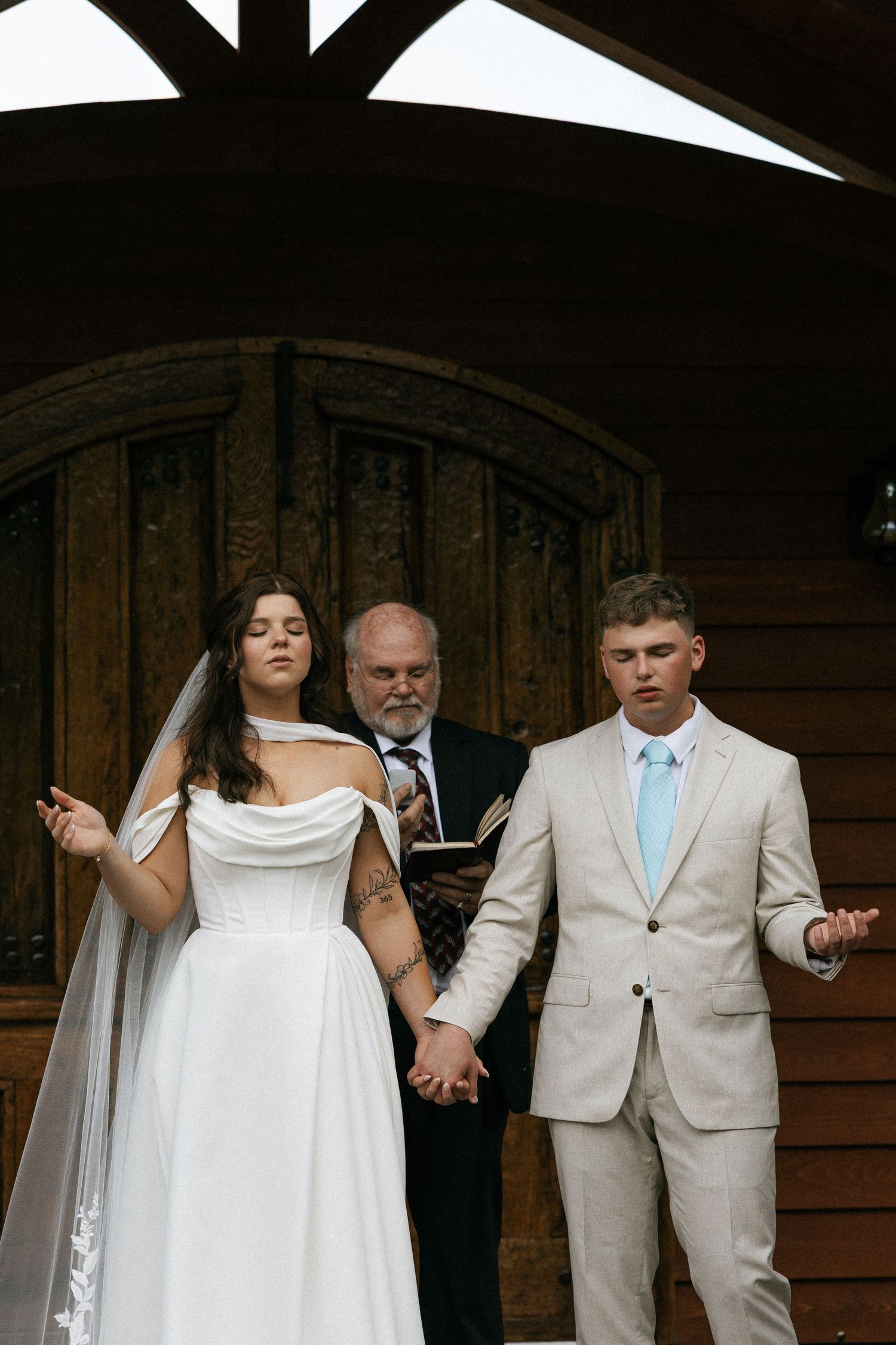 A couple holds hands during their wedding ceremony in front of a wooden door.