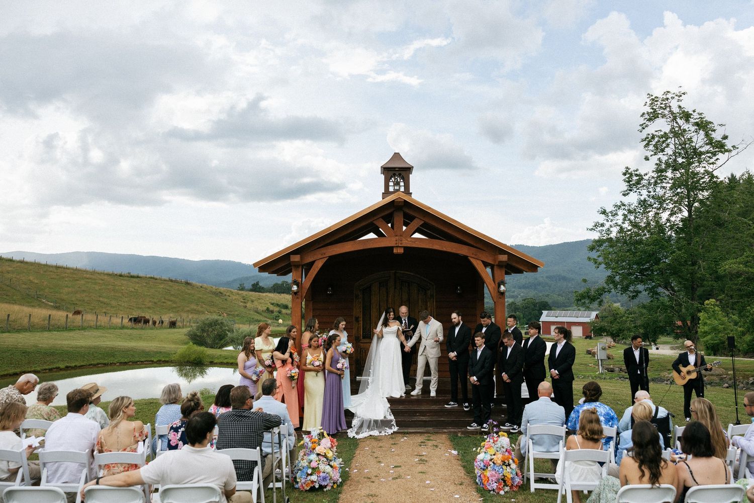 Panoramic view of an outdoor wedding venue with wooden pavilion and mountain scenery.