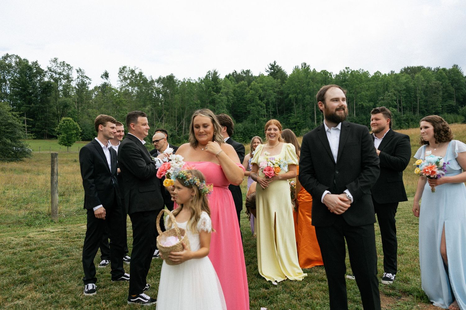 Wedding party in formal attire posing together on grassy field with trees in background.Micro wedding, elopement, intentional celebration