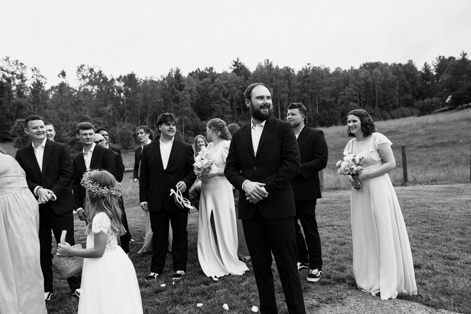 Wedding party in formal attire stands together in a black and white photo series outdoors on grassy field. Micro wedding, elopement, intenti
