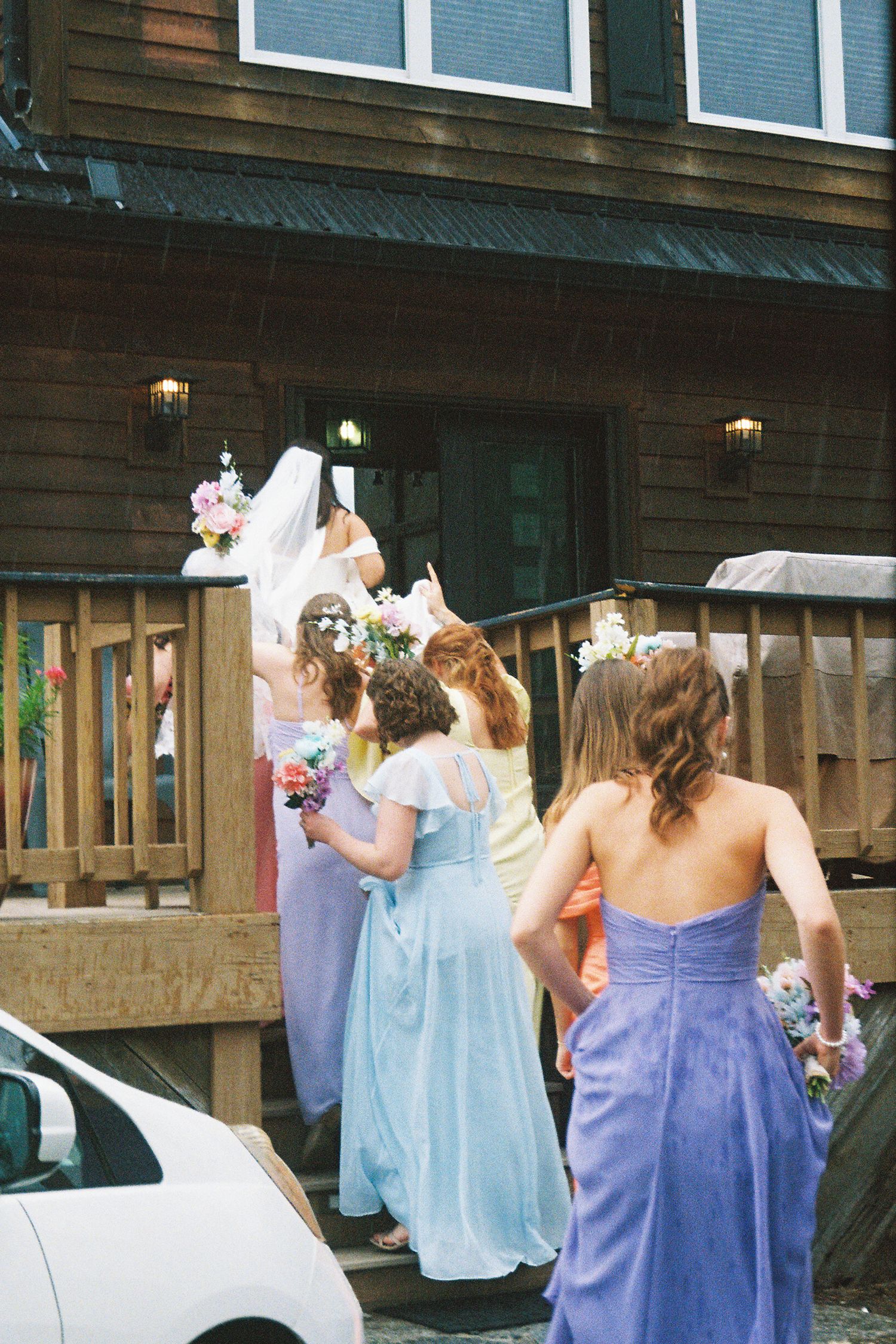 Bridesmaids in purple and light blue dresses pose together outside a rustic wooden building.Micro wedding, elopement, intentional celebratio