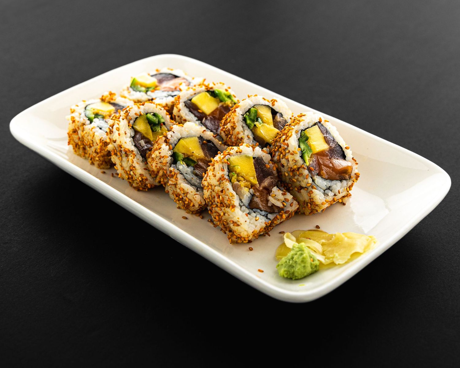 Sushi roll topped with grilled eel and avocado served on a white rectangular plate with wasabi garnish.