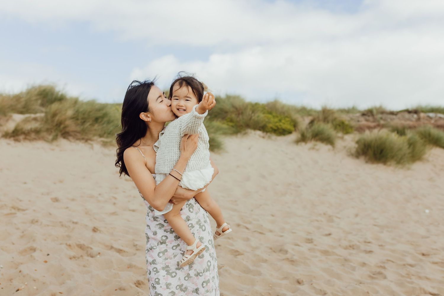 Mother holding their baby by the sea during a natural family photoshoot.