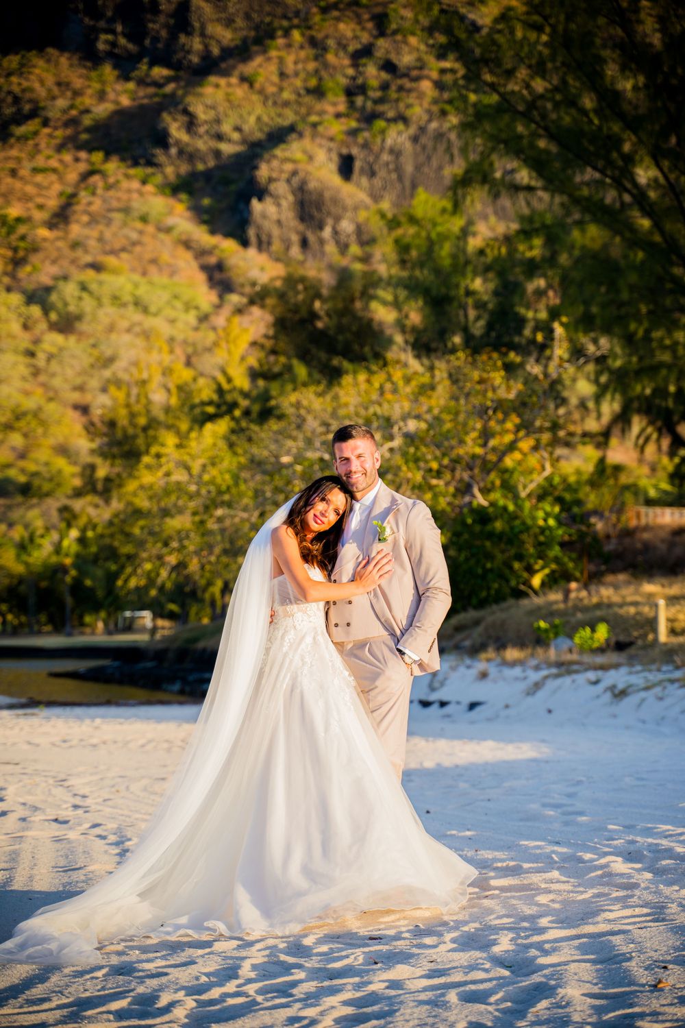 Newlyweds share intimate moments on a sandy beach with autumn foliage in the background.