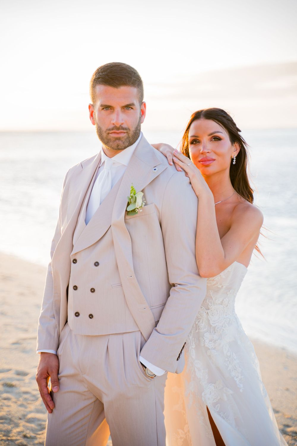 Wedding couple poses on beach in elegant white dress and beige suit.