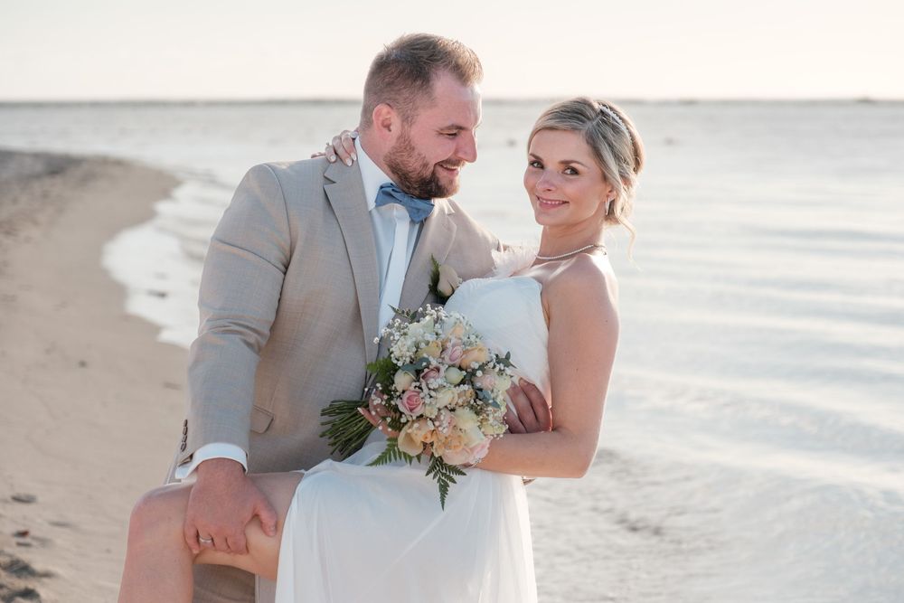 Beach wedding portraits with gentle waves and sandy shoreline in the background.