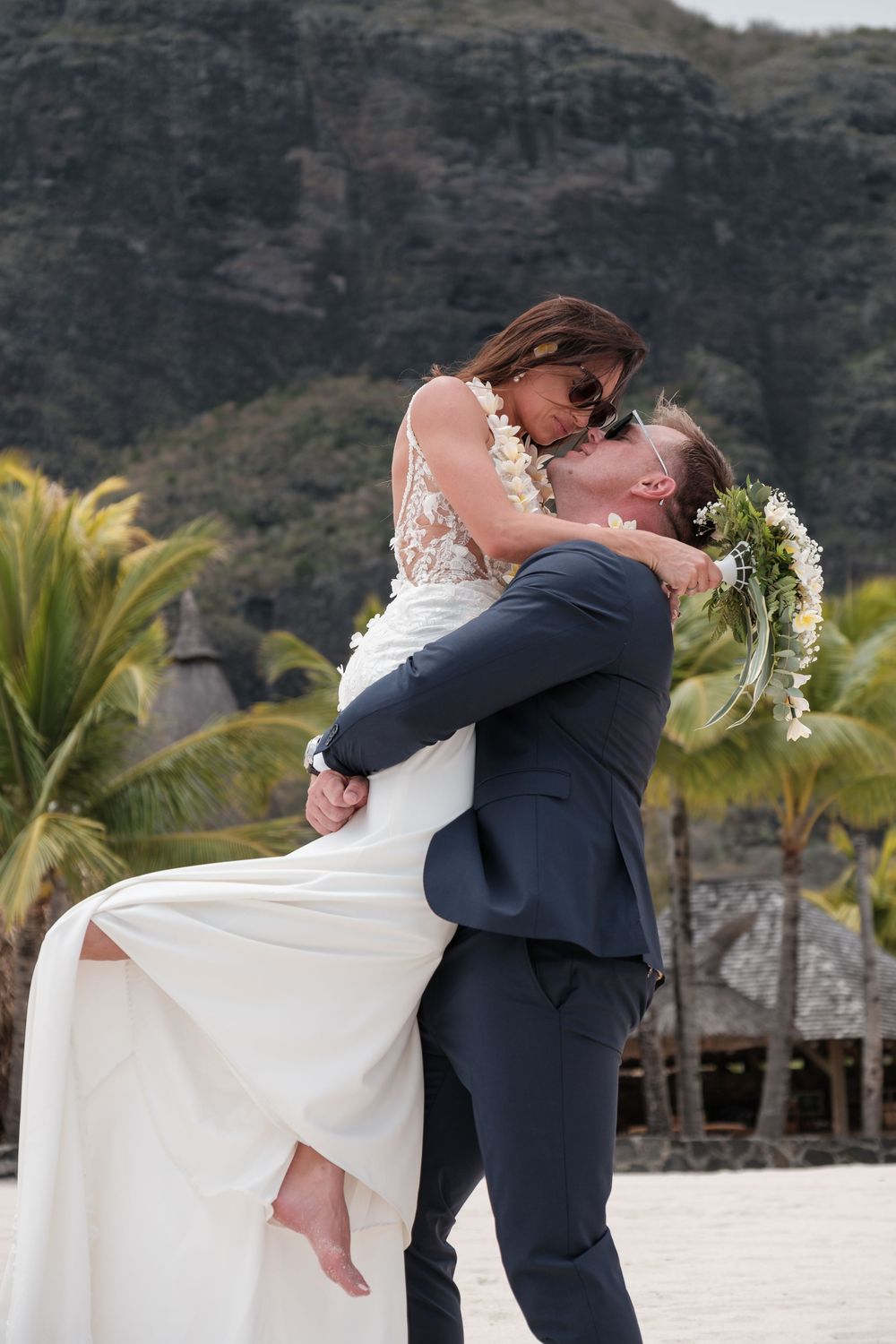 Romantic wedding dip kiss with mountain backdrop and tropical palm trees.