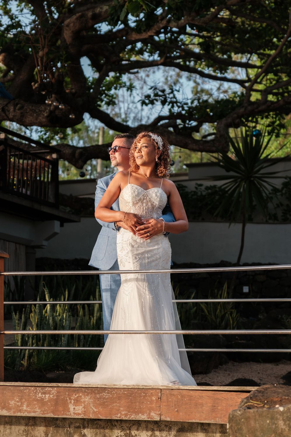Romantic sunset portrait of wedding couple embracing on wooden deck with tropical scenery.