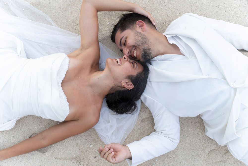 Couple in white attire lying on a white surface in a romantic photoshoot sequence.