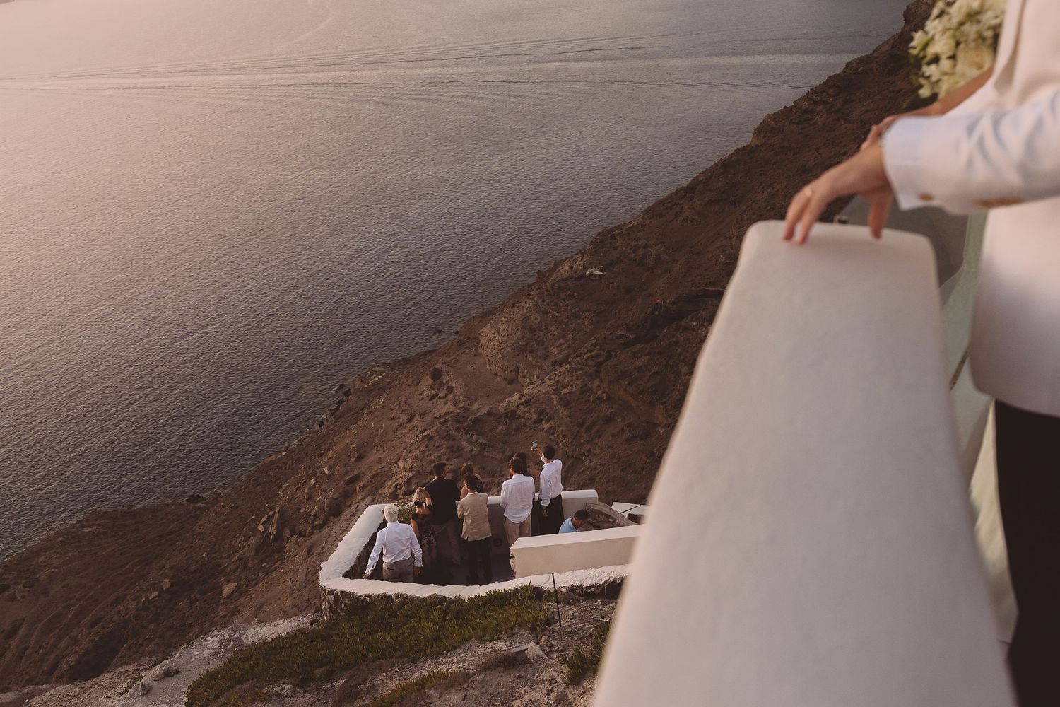 A destination wedding couple overlooking a cliffside ocean view during sunset in Santorini, Greece.