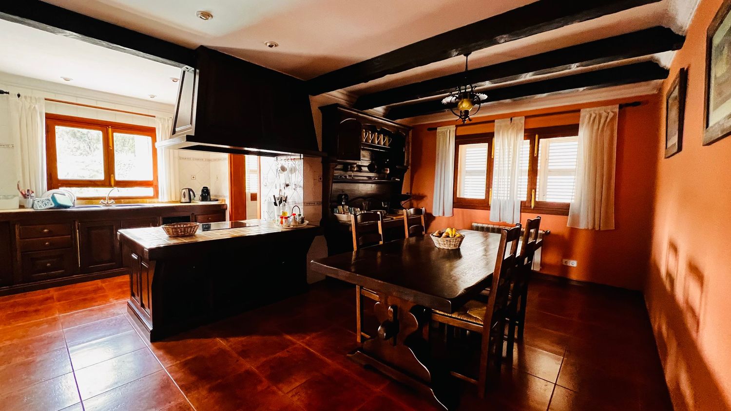 Rustic kitchen and dining area with dark wood beamed ceiling, terracotta tile floors, and traditional wooden furniture.