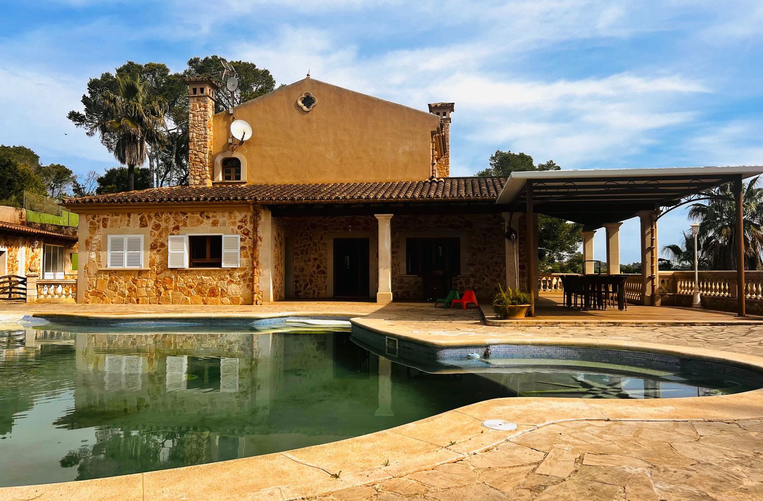 Mediterranean stone villa with outdoor swimming pool, pergola, and palm trees under a clear blue sky.