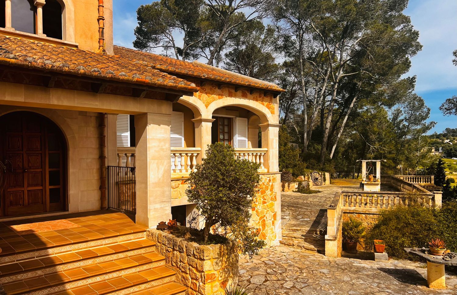 Elegant Mediterranean stone villa entrance with arched portico, terracotta roof tiles, and manicured garden staircase.