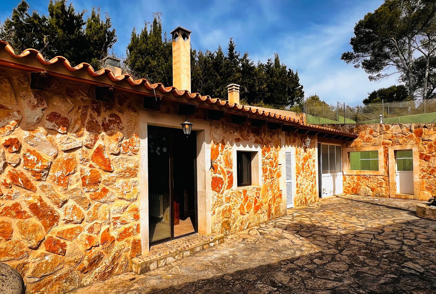 Traditional stone cottage exterior with terracotta roof tiles, wooden shutters, and lush green surroundings.