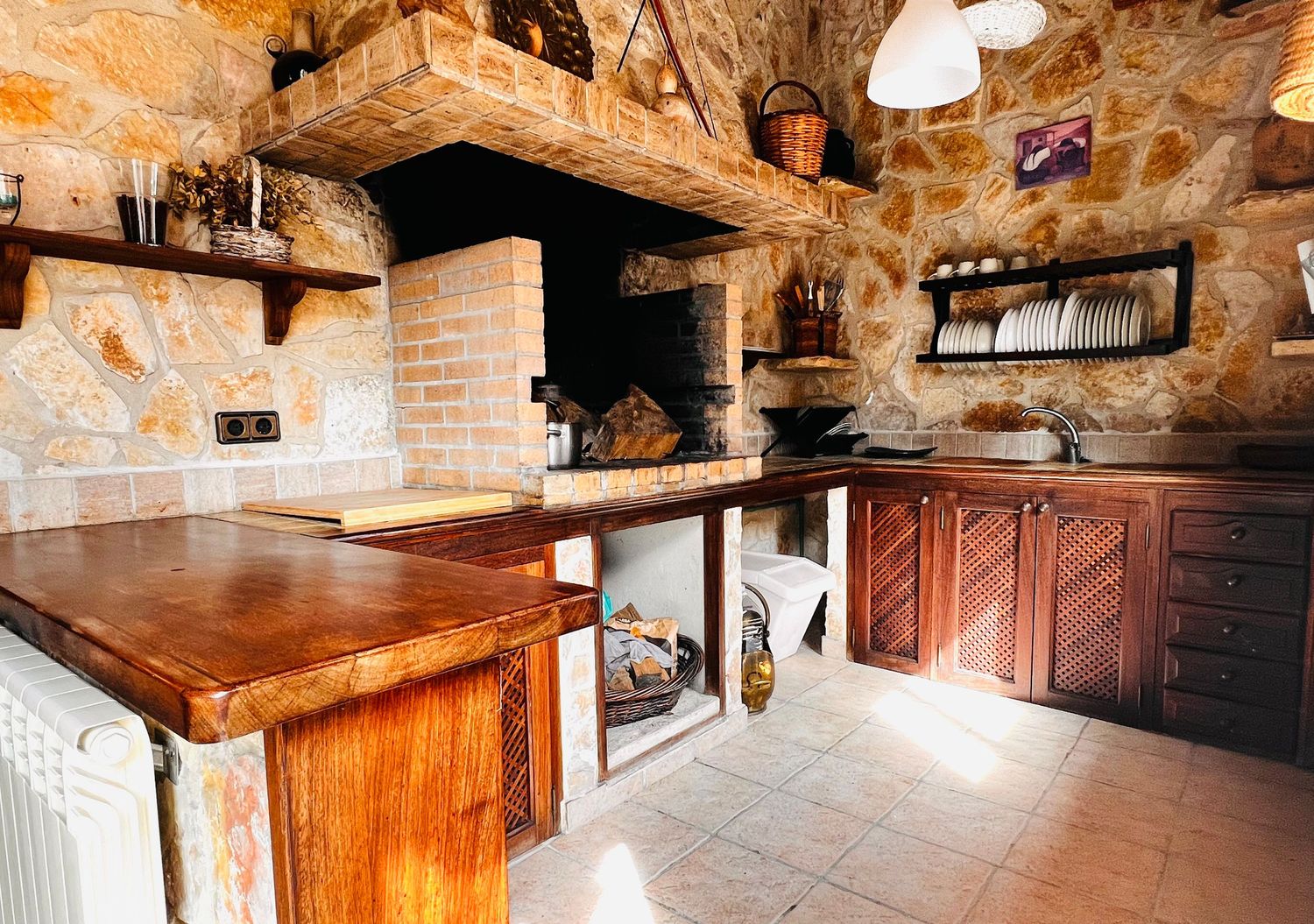 Rustic stone kitchen with wooden countertop, brick fireplace, and dark wood cabinets in a Mediterranean-style home.