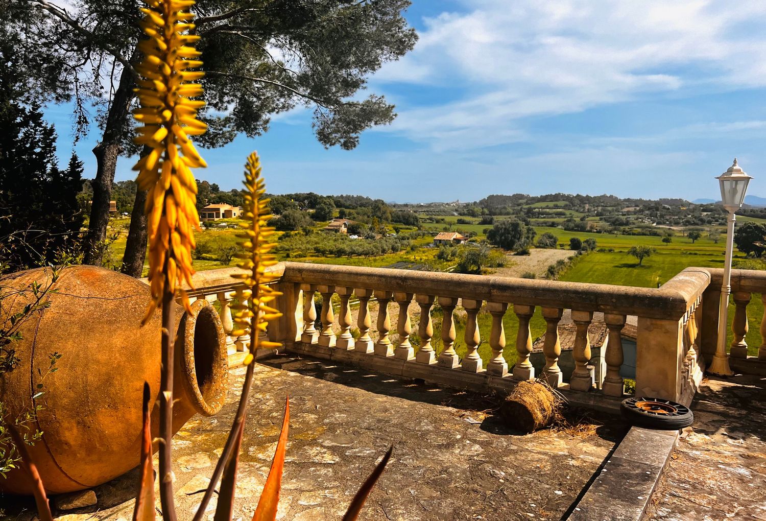 Scenic Mediterranean terrace with stone balustrade, clay pot, and panoramic countryside views.