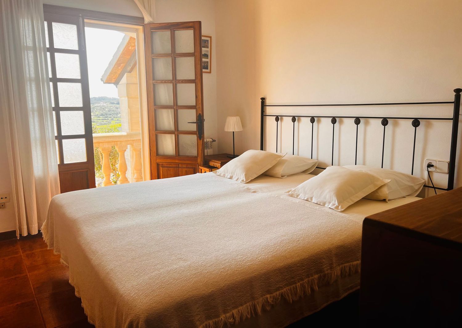 Bright bedroom with white bedding, wrought iron headboard, and open balcony doors offering scenic views and natural light.