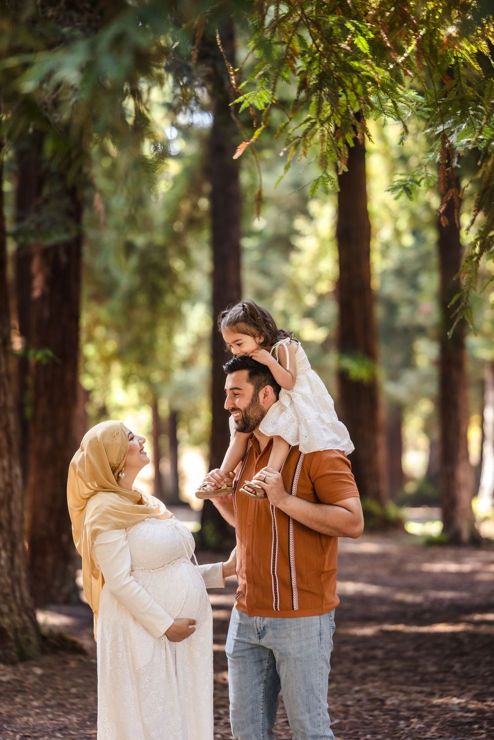 A couple shares intimate moments while walking through a sunlit forest with tall trees.