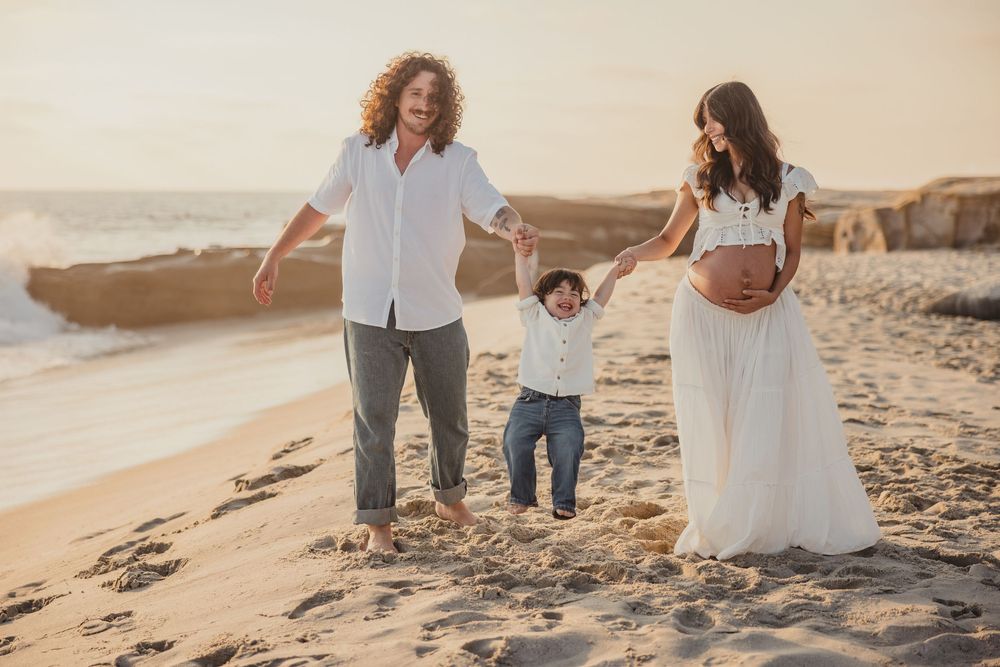 People enjoy a romantic moment while walking along the sandy beach at golden hour with scenic coastal cliffs in the background.