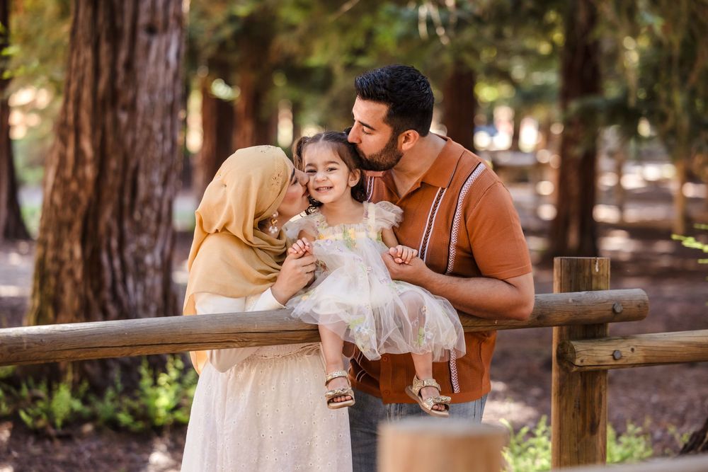 A joyful family wearing warm earth tones shares a tender moment together while leaning on a wooden railing outdoors.