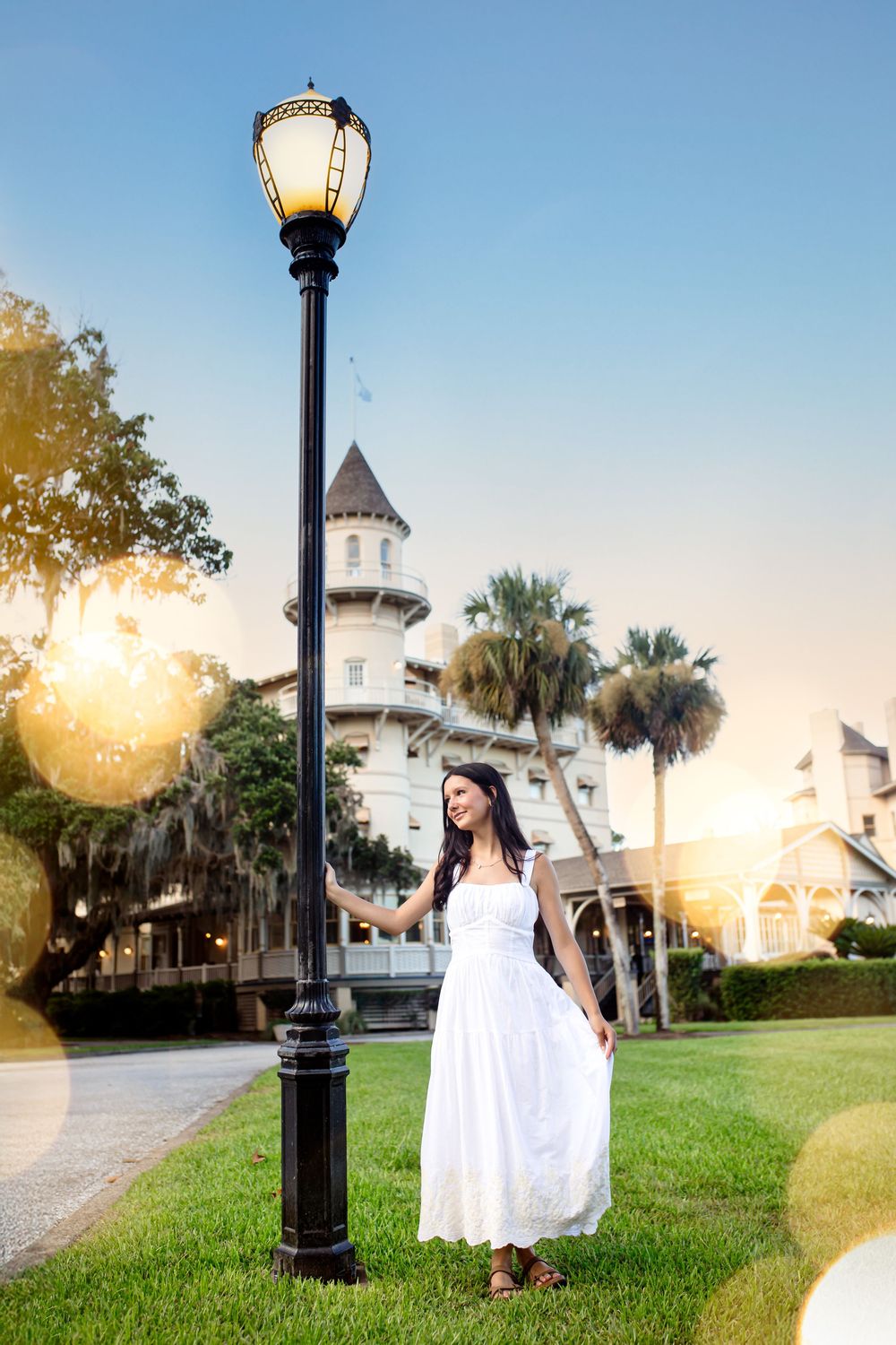 White dress near vintage lampposts at sunset creates dreamy scenes along a palm-lined pathway.