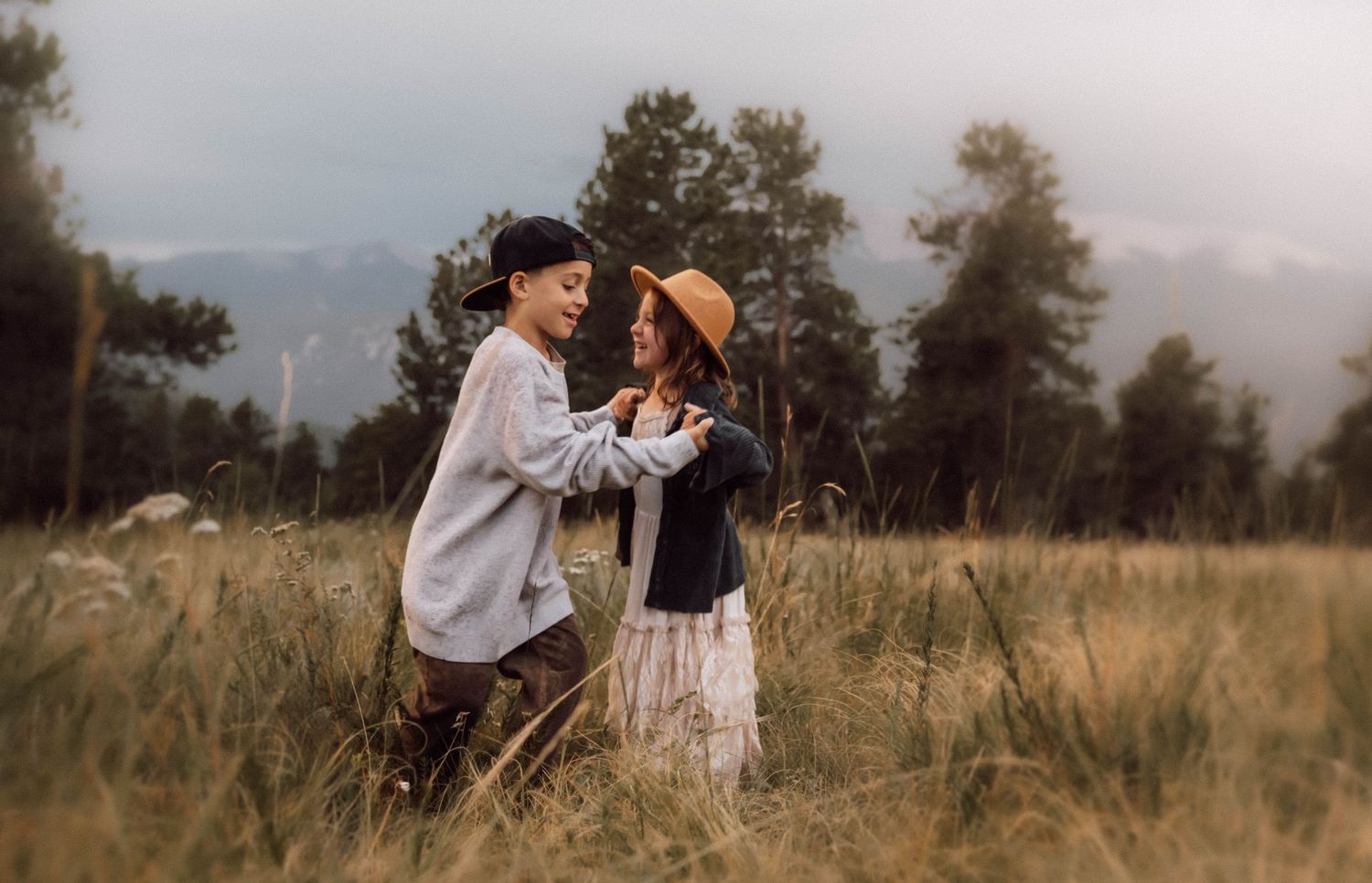Children dance and play while their father strums an instrument in tall grass with mountains behind them.