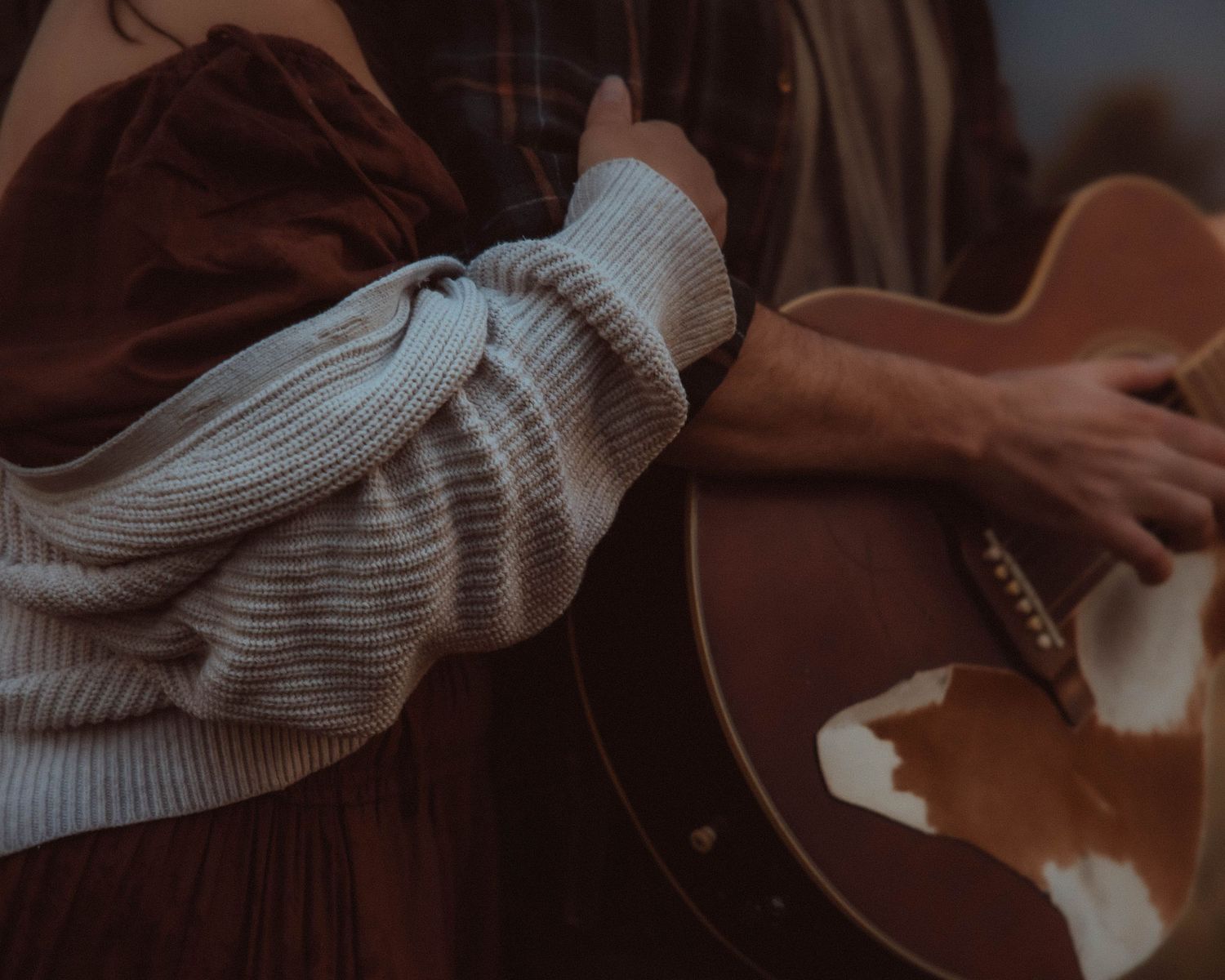 Close-up details of hands playing acoustic guitar while wearing white knit sweater.