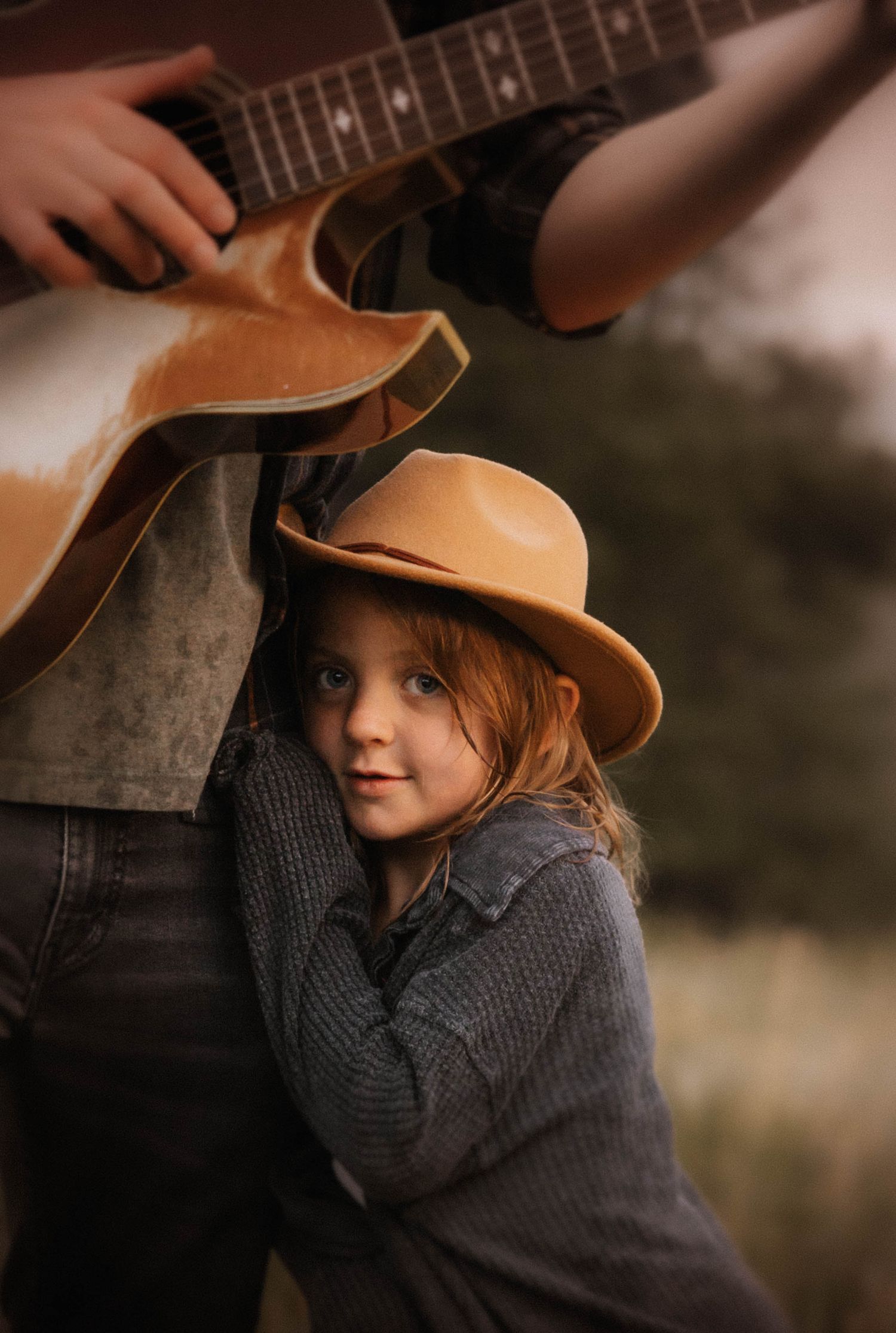 A child clung to the hip of her father while he plays her favorite song with he guitar.