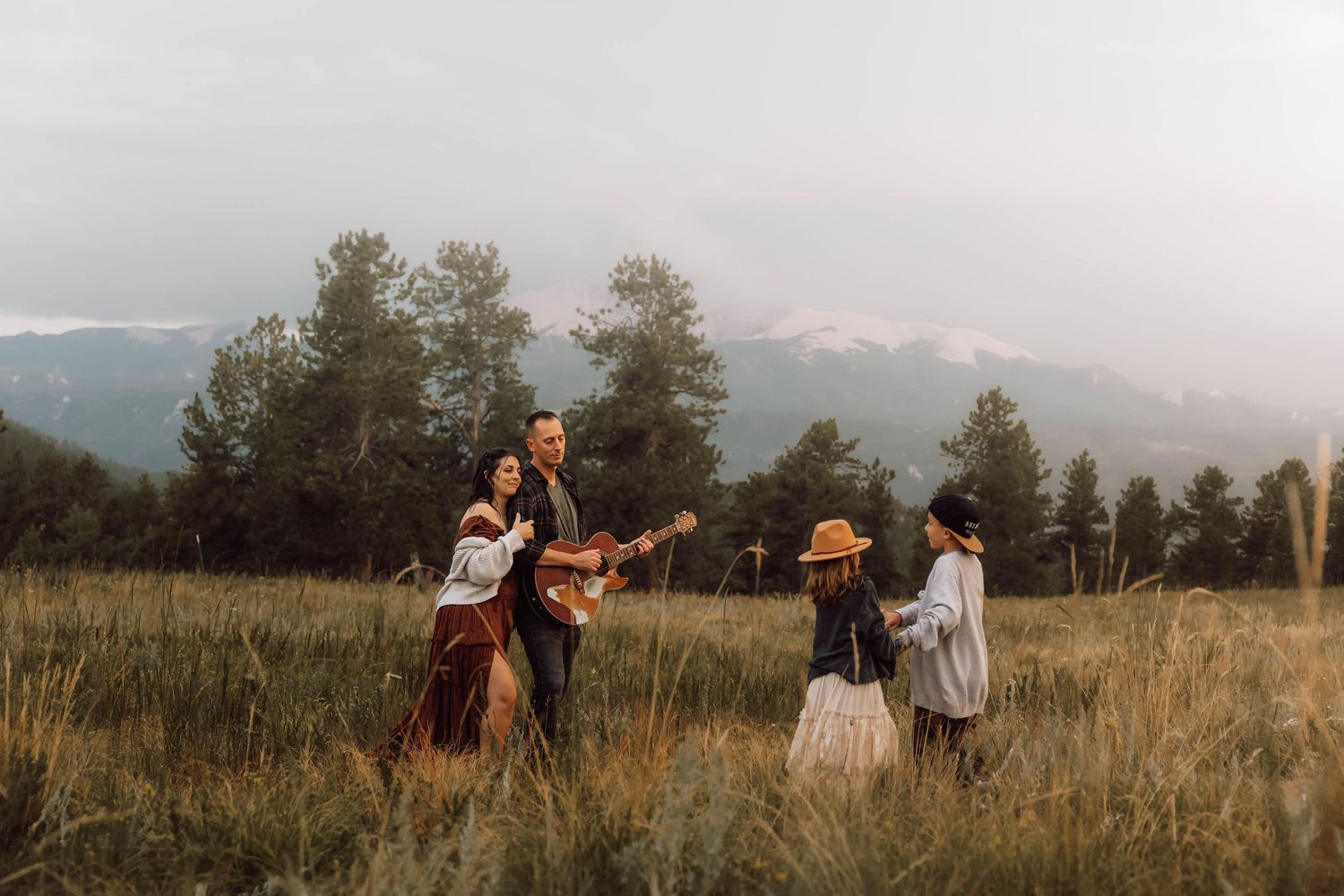 A family dances and sings in an open field with mountains in the background.