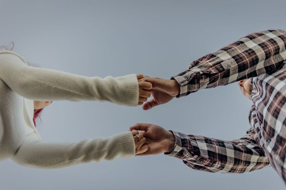 Two hands with wedding rings clasping together in front of a soft gray background.