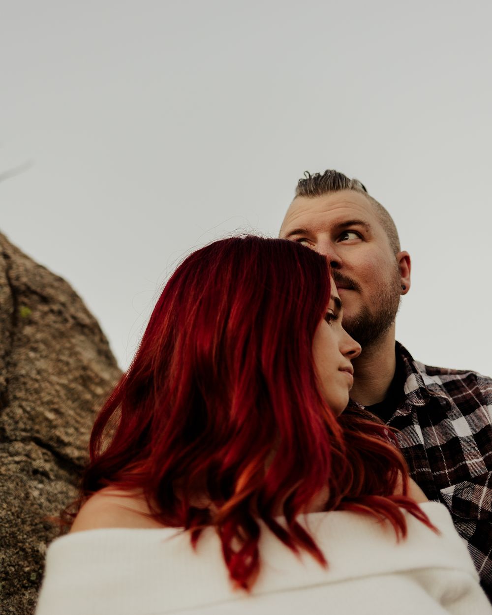 Artistic black and white portrait showing two people embracing intimately against a rocky outdoor backdrop.