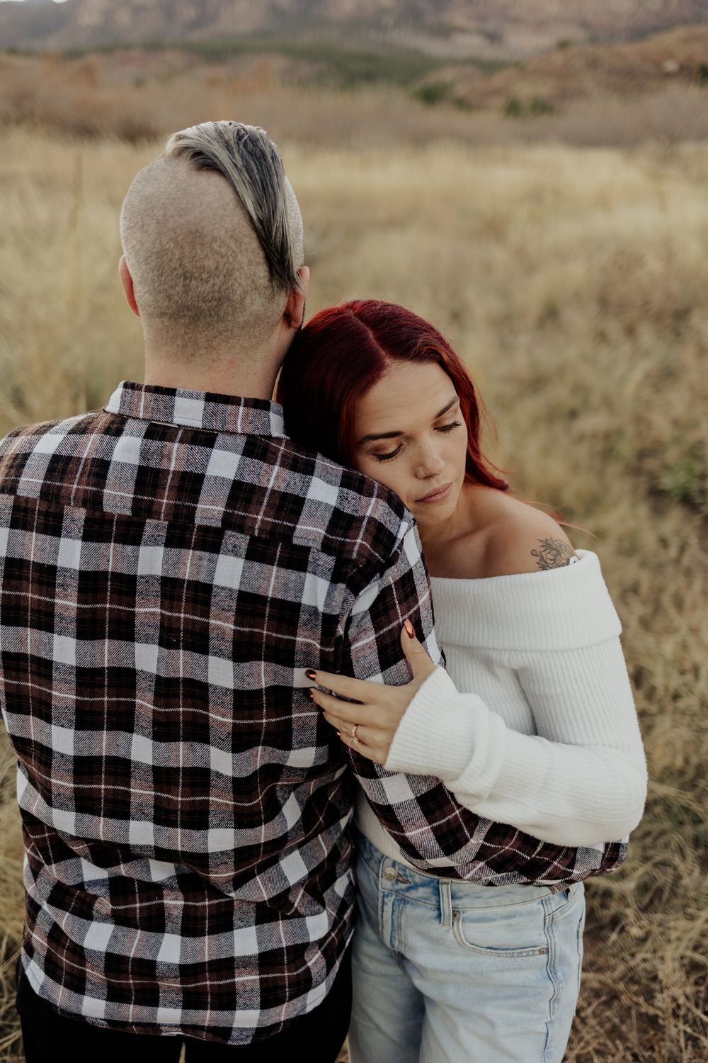 A couple sharing an intimate embrace in a field with mountains in the background.