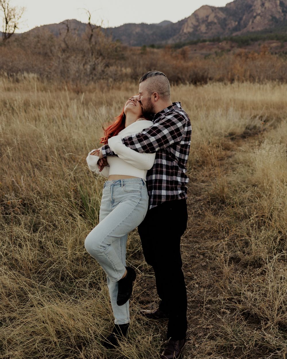 Playful couple dancing and twirling in a desert landscape with mountains in the background.